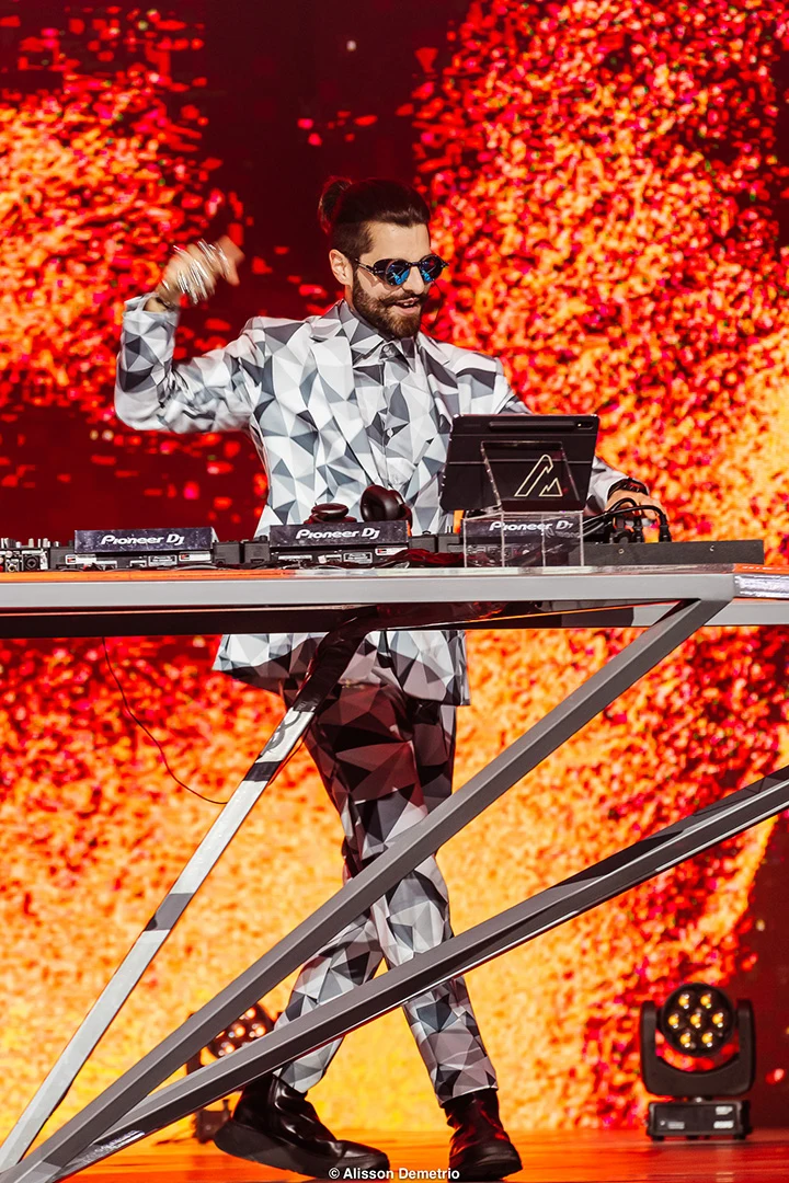 Alok at the decks, surrounded by glowing orange particles on the LED stage.