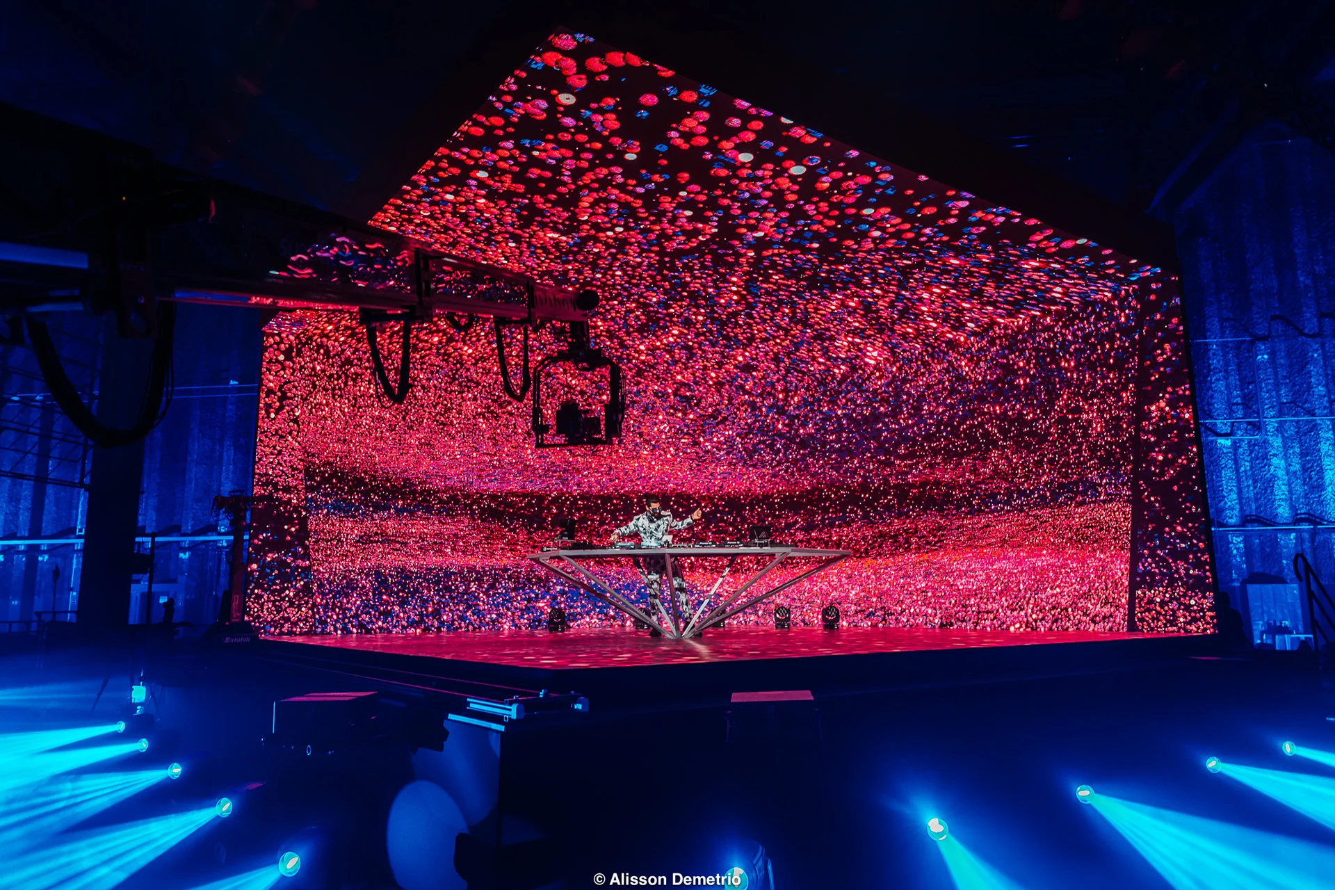 Alok performing inside the LED stage filled with pink generative particles, with the camera crane in the foreground.